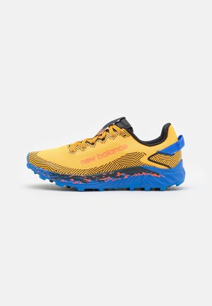 Geel en zwarte New Balance hardloopschoen met felblauwe zool en hieltreklipje, oranje logo aan de zijkant en patroonrijke details op het bovenwerk.