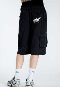 Pantaloni cargo neri con vita elasticizzata, due grandi tasche laterali e logo "M" ricamato bianco a contrasto. Tessuto liscio e leggero.