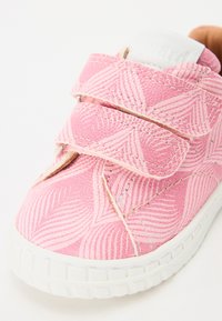 Różowe sneakersy z teksturowanym wzorem falistych linii, wyposażone w rzepy oraz białą gumową podeszwę. Zawierają wyściółkę wokół kostki.