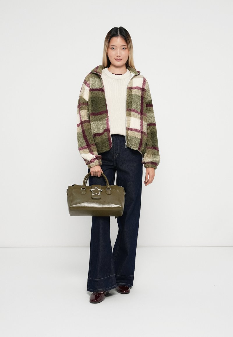 Giacca oversize a scacchi con toni verdi, bianchi e borgogna, indossata sopra un maglione color crema. Jeans ampi scuri e borsa oliva con dettaglio a stella.