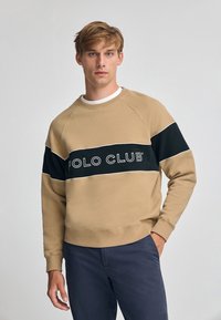Felpa beige con una banda orizzontale nera etichettata "POLO CLUB" in bianco. Presenta maniche raglan e un materiale a trama di cotone misto.
