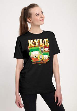 Młoda kobieta w czarnej koszulce z kolorowymi postaciami z kreskówek i napisem "KYLE" z South Park.
