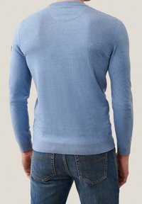Maglione azzurro chiaro lavorato a maglia con maniche lunghe, scollo rotondo e polsini a costine. Abbinato a jeans blu scuro, che mostrano una vestibilità rilassata e una texture interessante.