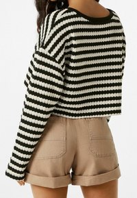 Pull en maille rayé noir et blanc avec un design court et une coupe décontractée, associé à un short beige retroussé avec poches arrière.