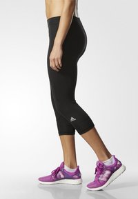 Czarne legginsy capri z elastycznego materiału, w połączeniu z purpurowymi butami sportowymi z siateczkowymi akcentami i białymi podeszwami.