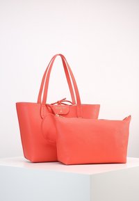Torebka na ramię z korygowanym skórzanym wykończeniem w kolorze koralowym, z dwiema rączkami, z możliwością ściągnięcia na sznurku oraz dopasowaną torebką na zamek. Gładka tekstura, minimalna ilość metalowych elementów.