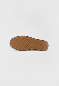 Suela de calzado negra con un diseño texturizado y un patrón en relieve del logo de Michael Kors en color marrón. Forma plana y ligeramente curvada.
