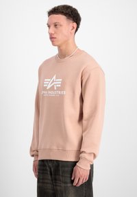 Sudadera rosa claro con puños y dobladillo acanalados. Presenta un logotipo blanco prominente en el frente. Fabricada con un tejido suave y texturizado.