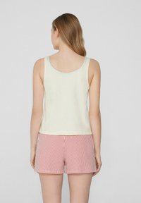 Débardeur jaune clair avec des coutures contrastées bleues et roses, associé à un short à rayures rouges et blanches. Tissu lisse, design décontracté.