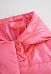 Różowa satynowa tkanina, z delikatnie zgromadzonym wzorem, o gładkiej fakturze i widocznym szyciu, tworząca subtelny blask.