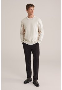 Sweat-shirt beige clair à col rond, associé à un pantalon foncé. Le pantalon présente une texture lisse, et une paire de chaussures en cuir noir complète la tenue.