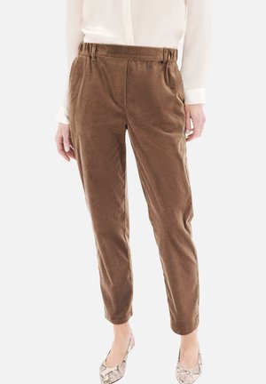 Pantalons en velours côtelé marron avec une taille élastique, présentant un ribbing vertical et une coupe jambe fuselée, associés à un chemisier léger.