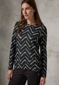 Svart och vit topp med zigzag-mönster, lång ärm och rund halsringning samt justerbart knytband i midjan. Mjuk textur.