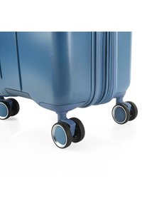Maleta rígida azul con superficie texturizada, que cuenta con ruedas dobles con detalles en cromo y un cierre resistente.