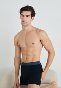 Schwarze Boxershorts mit einem grauen Calvin Klein Bund. Der Stoff wirkt weich und elastisch, und das Design ist minimalistisch und körperbetont.