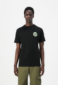 Black cotton t-shirt with short sleeves featuring a green and white "Santa Cruz" logo printed on the left chest. Simple and classic design.