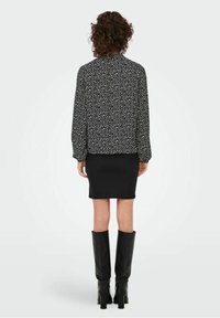 Zwarte blouse met patroon van witte stippen, lange pofmouwen en een hoge kraag, gecombineerd met een nauwsluitende zwarte rok en zwarte laarzen tot aan de knie.