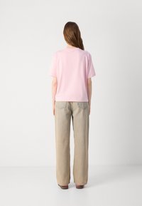 T-shirt di cotone rosa chiaro con maniche corte e vestibilità ampia, abbinato a pantaloni beige a vita alta con gambe larghe e tasche frontali.