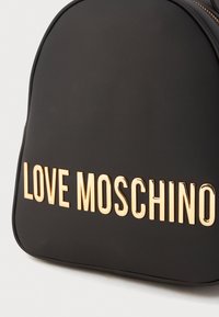 Schwarzer Kunstleder-Rucksack mit abgerundeter Oberseite, goldener "LOVE MOSCHINO" Schriftzug in fetter Schriftart und einem Reißverschluss entlang der Kante.