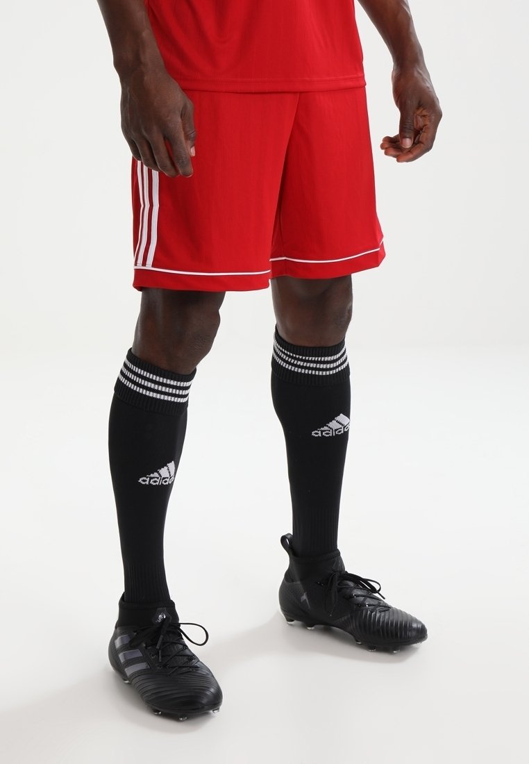 Shorts de football rouges avec des rayures blanches, associés à des chaussettes noires hautes avec des accents rayés et des crampons de football noirs.