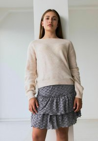 Pull beige clair à manches longues associé à une jupe grise à volants présentant un motif floral texturé. Design simple et moderne.