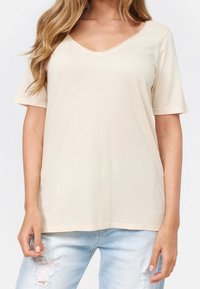 Bežové tričko s výstřihem do V vyrobené z měkké bavlny, s krátkými rukávy a volným střihem. Texturovaná látka bez viditelných vzorů nebo akcentů.