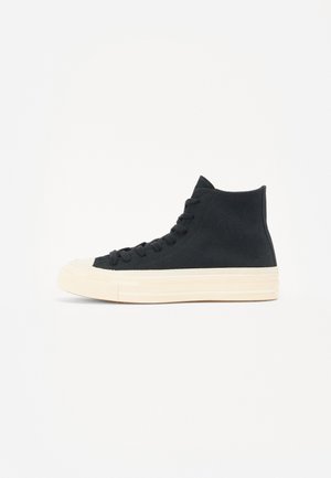 Baskets montantes noires en toile avec semelle et bout en caoutchouc blancs, vues de profil sur fond blanc.