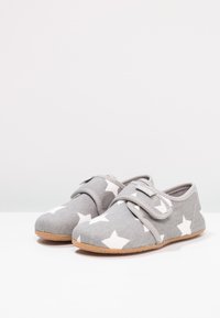 Chaussures en tissu gris avec motifs d'étoiles blanches, dotées d'une fermeture à bande Velcro et d'une semelle texturée pour une meilleure adhérence. Doublure intérieure lisse.