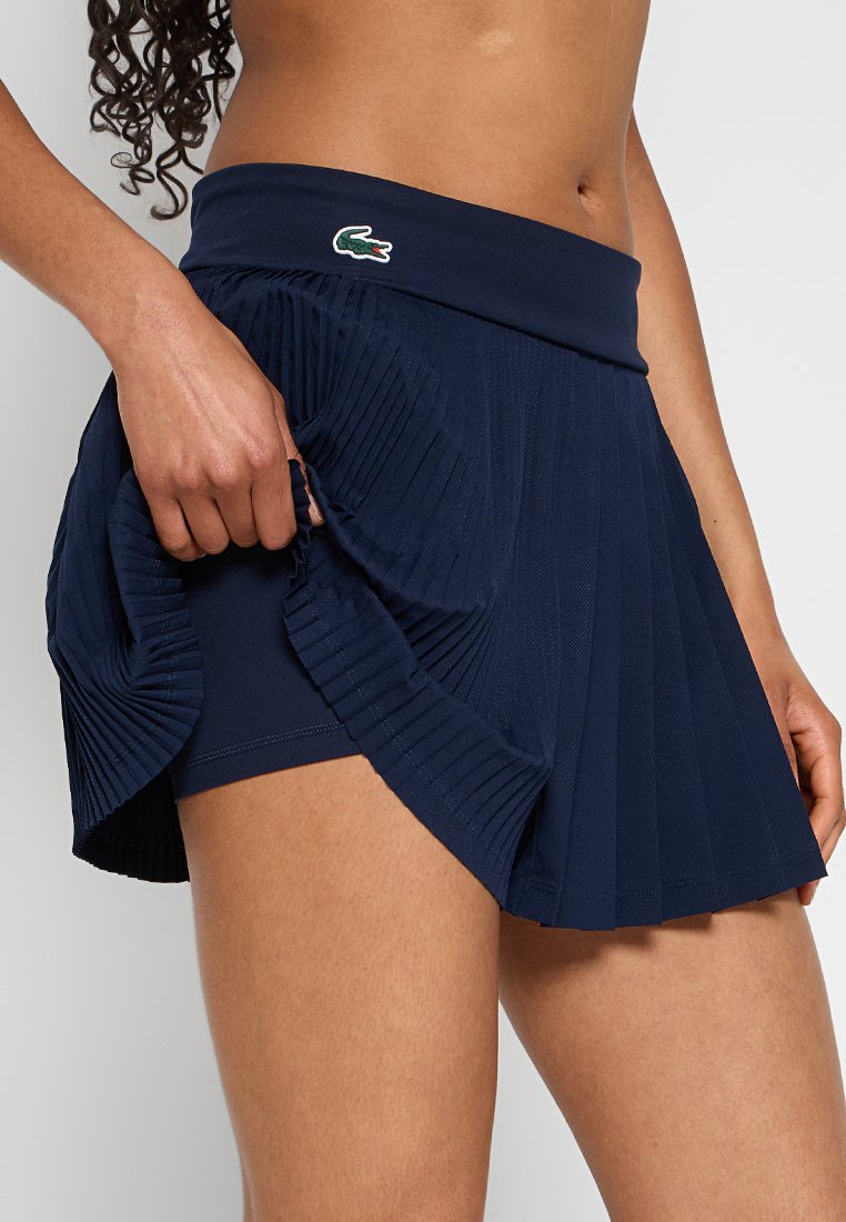 Granatowa plisowana spódnica z elastycznym paskiem, wykonana z teksturowanej tkaniny, z małym zielonym logo na pasku.