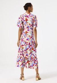 Vestido midi de estampado floral colorido con mangas cortas abullonadas y dobladillo con volantes, hecho de una tela ligera. Lleva unas sandalias de tacón doradas.