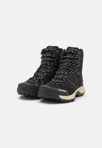 Black hiking boots with textured fabric, reinforced toe, and rubber outsole. Features heavy-duty laces and a beige midsole.