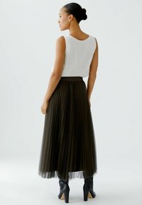 Black pleated tulle skirt with a textured waistband, paired with a white sleeveless top. Model wearing black heeled boots.