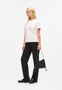 T-shirt crème avec un motif imprimé, associé à un pantalon noir, des mocassins ornés et un sac à main noir texturé avec une bandoulière en chaîne.