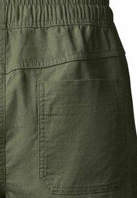 Gros plan sur un tissu vert olive montrant une poche arrière carrée avec double couture et une ceinture élastique au-dessus.