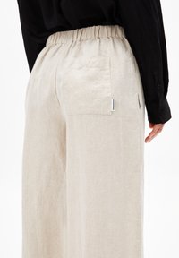 Helle beige Leinenhose mit elastischem Bund und Seitentasche. Die Textur ist weich mit einem leicht zerknitterten Aussehen.