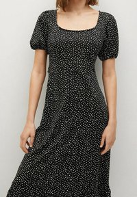 Czarna sukienka w kropki z krótkimi bufkami, kwadratowym dekoltem, dopasowaną talią i swobodną spódnicą. Wykonana z lekkiego materiału o gładkiej fakturze.