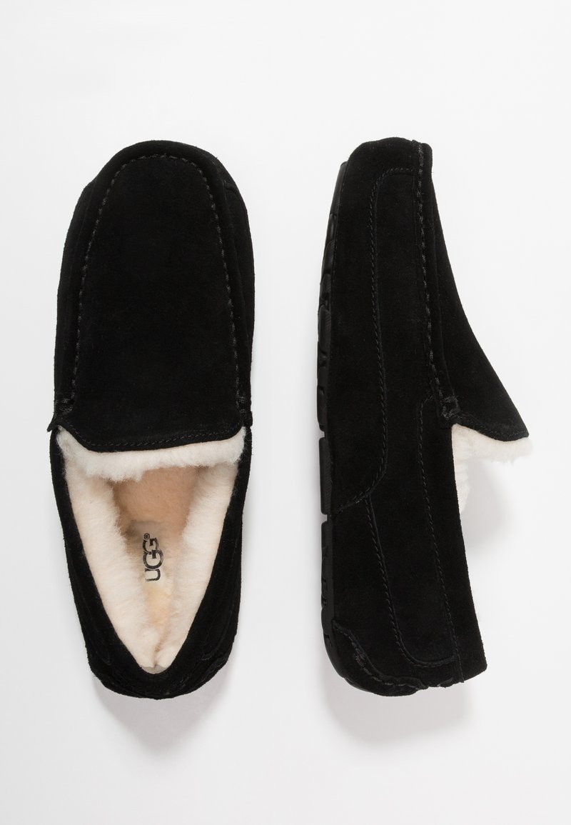 Black suede slippers with plush cream fur lining, rounded toe, and textured black rubber sole. Visible stitching along edges.
