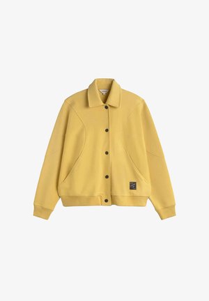 Gelbe Button-up-Jacke mit Kragen, langen Ärmeln, seitlichen Taschen, gerippten Bündchen und Saum sowie einem kleinen schwarzen quadratischen Logopatch nahe dem unteren Saum.