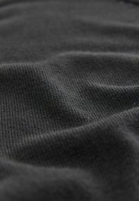 Svart texturerat tyg med ett mjukt, ribbat mönster. Ytan verkar slät med lätta vågor, vilket indikerar ett lätt material.