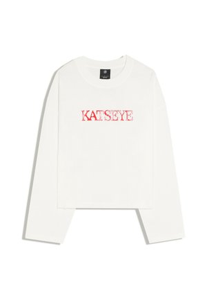 Weißes langärmliges kurz geschnittenes Shirt mit rotem Text "KATSEYE" auf der Brust, dargestellt auf weißem Hintergrund.