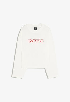 T-shirt court blanc à manches longues avec texte rouge "KATSEYE" imprimé sur la poitrine, présenté sur un fond blanc uni.