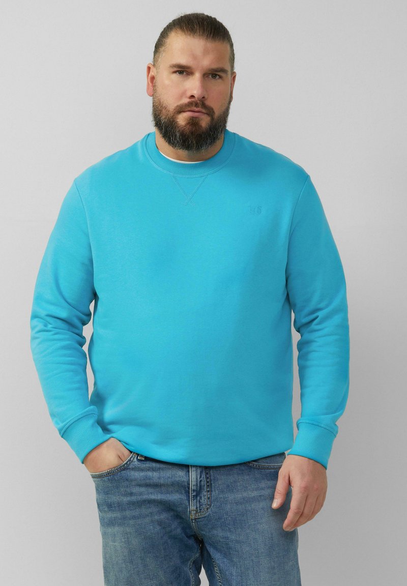 Türkisfarbener Sweatshirt mit langen Ärmeln und Rundhalsausschnitt; aus einem weichen Baumwoll-Mix gefertigt. Verfügt über ein minimalistisches Logo auf der Brust; kombiniert mit blauen Jeans.