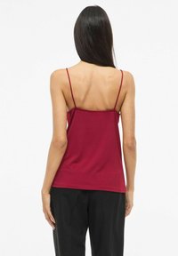 Burgundowa koszulka na cienkich ramiączkach, o gładkiej fakturze, luźnym kroju i wycięciu na plecach w kształcie litery U. W zestawie z czarnymi, luźnymi spodniami.