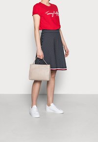 Röd bomullströja med vitt logo, marinrandig A-linjeformad kjol, vita sneakers och beige handväska med ett handtag.