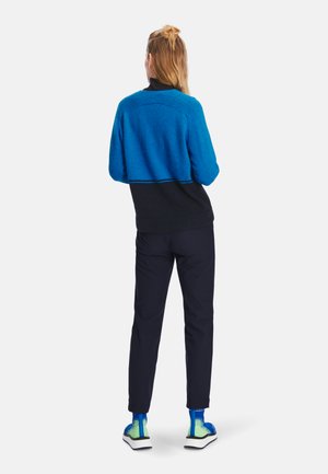 Blauer und schwarzer Pullover mit strukturierter Oberfläche, kombiniert mit marineblauen Hosen und mehrfarbigen Turnschuhen mit einem Farbverlaufsmuster an den Seiten.