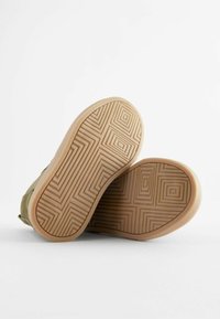 Soli de adidași din țesătură verde cu un fund de cauciuc texturat de tip gumă, având un model geometric și linii unghiulare, prezentând detalii de pe partea de jos.