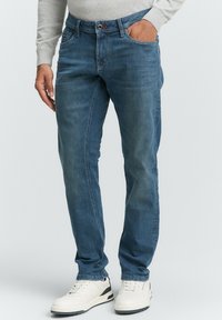 Blauwe denim jeans met een lichte vervaging, rechte pasvorm, vijf zakken en een knoopsluiting, gecombineerd met witte sneakers.