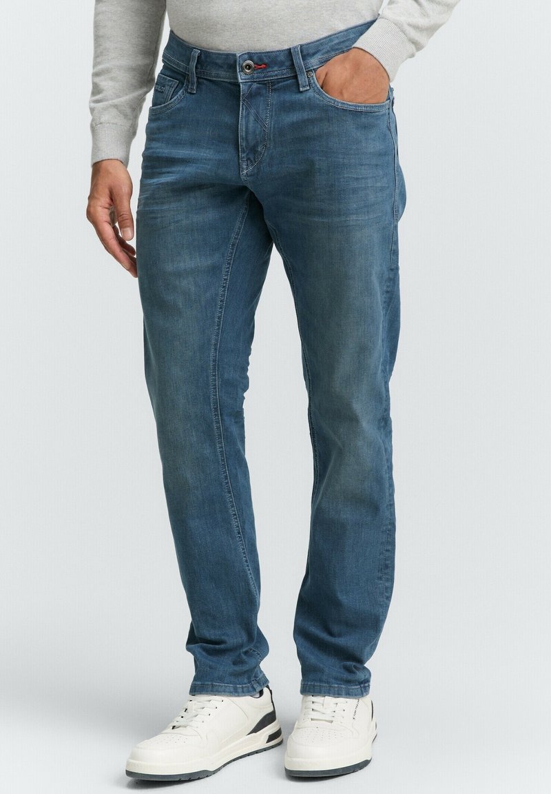 Blauwe denim jeans met een lichte vervaging, rechte pasvorm, vijf zakken en een knoopsluiting, gecombineerd met witte sneakers.