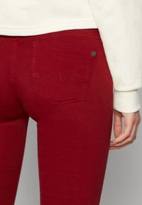 Červené džíny se slim střihem a zadní kapsou s dekorativním prošitím. Materiál se zdá být hladký a pružný.