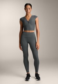 Top corto grigio a coste con maniche corte e dettagli a bottoni, abbinato a leggings grigi a vita alta. Scarpe sportive nere completano il look.